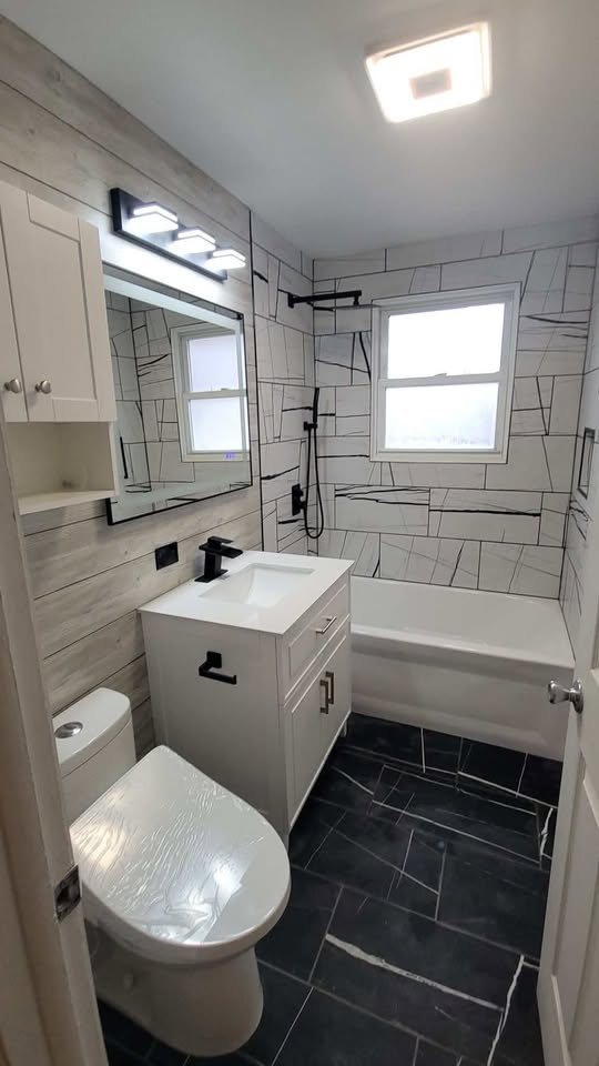 Bathroom with large-format marble-look wall tile, black fixtures, white vanity and dark tile floor